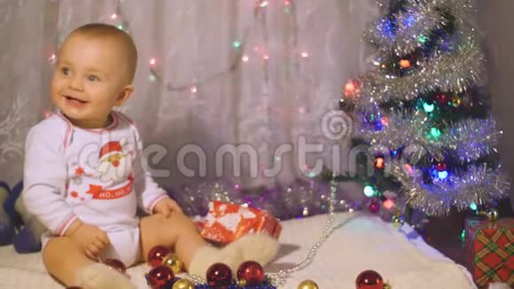 穿着圣诞老人睡衣的婴儿在圣诞树附近玩耍带着礼物幼儿新年概念视频的预览图