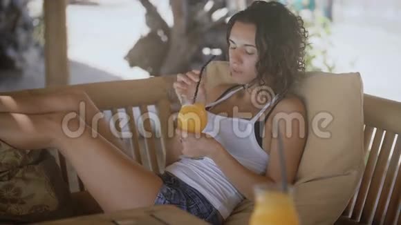 年轻的黑发女士在日光浴的帐篷下放松夏天她的手里拿着热带鸡尾酒女性视频的预览图