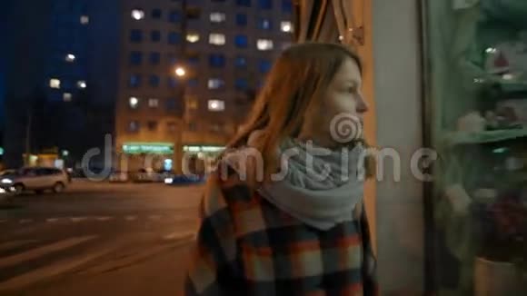 年轻女子在夜晚漫步穿过商店橱窗装饰和鲜花视频的预览图