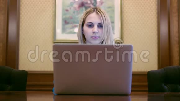 漂亮的女人坐在办公室的桌子上看着笔记本屏幕视频的预览图