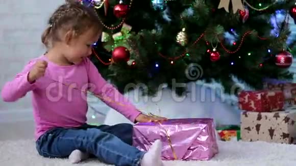 小女孩在圣诞树附近打开礼物盒儿童撕纸礼品视频的预览图