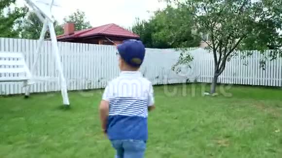 夏天一个四岁的男孩赤脚在一片绿色的草坪上草地上院子里慢跑开心开心视频的预览图