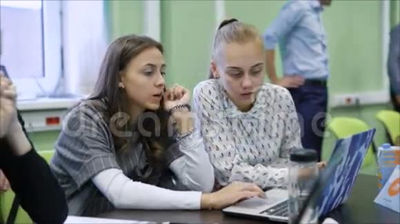 在教室里漂亮的女大学生坐在一起用电脑做视频的预览图