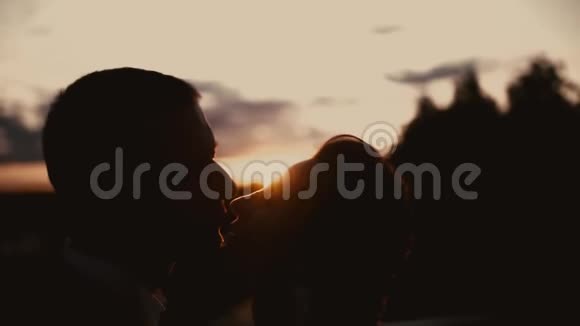 新婚夫妇在夕阳下拥抱亲吻的剪影视频的预览图