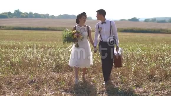 幸福的新婚夫妇牵着手在春田里散步穿着考究的新娘拿着花束视频的预览图