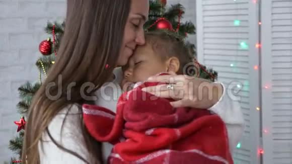 年轻的母亲牵着她熟睡的小女儿在圣诞树附近视频的预览图