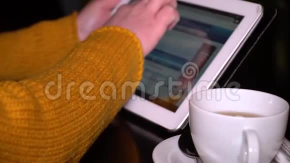 年轻女孩坐在餐桌旁的咖啡馆里用平板电脑这个女孩正在修改社交网络双手特写视频的预览图