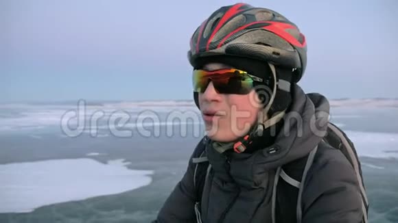 人是站在冰上的自行车他看着美丽的日落骑自行车的人穿着灰色的羽绒服背包视频的预览图