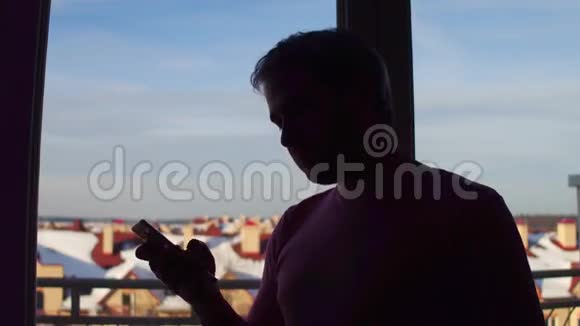 一个人在大窗户附近用手机的剪影冬季风景背景4K特写镜头视频的预览图
