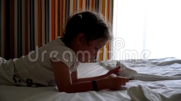 小女孩在平板电脑里的床上玩视频的预览图