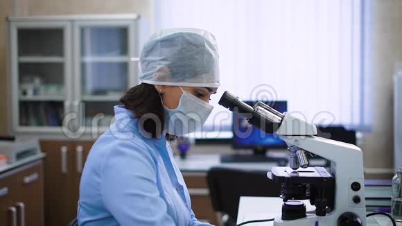 一位留着黑色短发的女性实验室助理穿着蓝色长袍在显微镜下检查病人检查视频的预览图