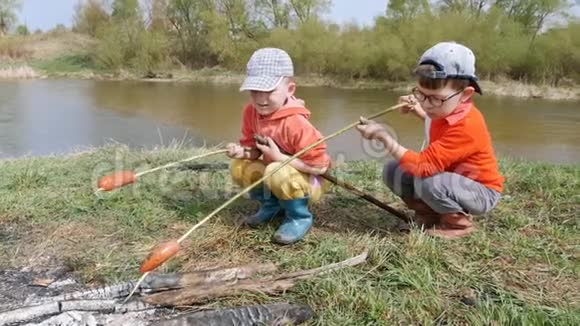 两个小男孩在一条快河的河岸上用煤烤香肠视频的预览图