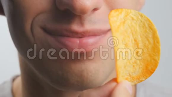 一个年轻人在白色背景下愉快地吃薯片的特写镜头视频的预览图