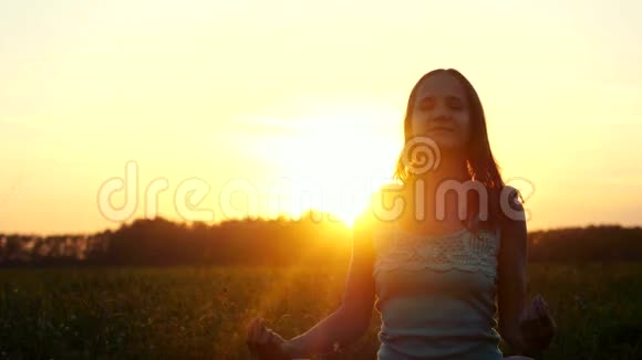 年轻美丽的黑发女人在令人惊叹的日落中冥想并有太阳耀斑的效果3840x2160视频的预览图