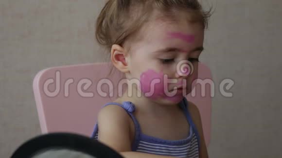 三岁的金发碧眼的婴儿在照镜子时脸上画着彩色条纹视频的预览图