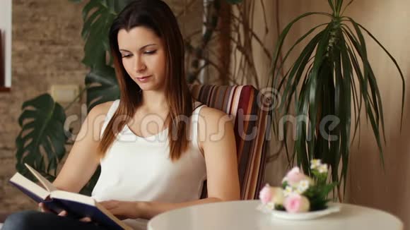 年轻迷人的女人在客厅里坐在舒适的椅子上读有趣的书视频的预览图