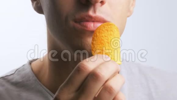 一个年轻人在白色背景下愉快地吃薯片的特写镜头视频的预览图