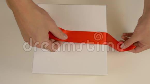 包装白色礼品盒高加索人手拿包装礼盒男人用手在一个白色的纸板箱周围系上一条红丝带视频的预览图