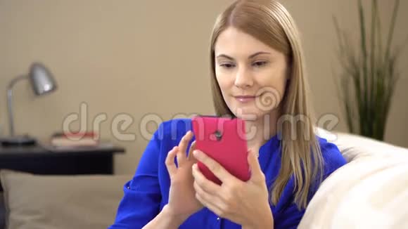 美丽迷人的年轻女子穿着蓝色t恤坐在沙发上打电话视频的预览图