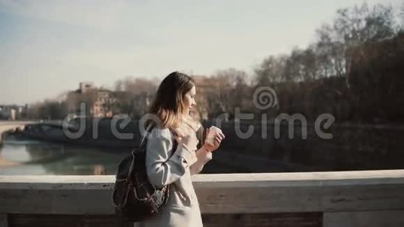 年轻漂亮的女人在阳光明媚的早晨在桥上散步迷人的女性喝咖啡散步视频的预览图