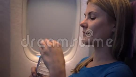 飞机窗户附近美丽迷人的女人长途飞行瓶装饮用水视频的预览图