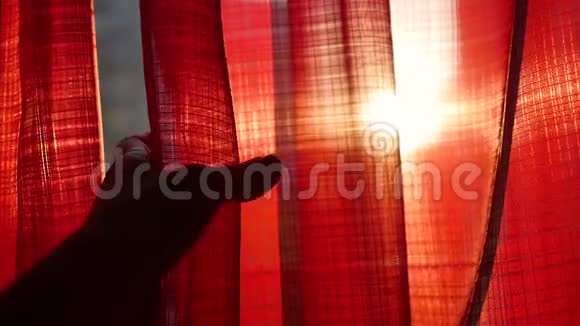 女孩打开红色的窗帘用手在阳光的光线下玩耍手工特写视频的预览图
