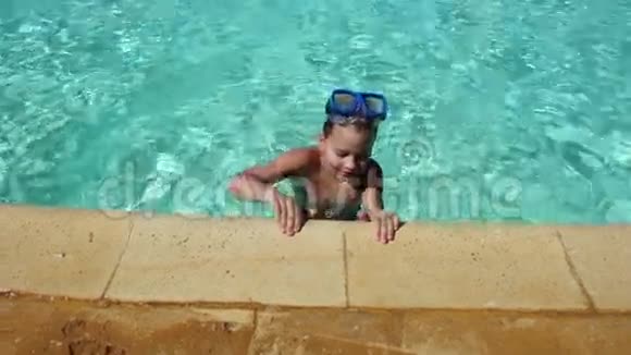 戴着游泳面罩的微笑男孩从蓝色游泳池出来视频的预览图