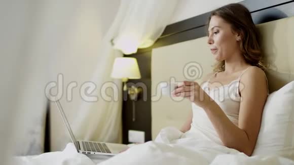 美女在床上喝咖啡时在笔记本电脑上做视频翻译视频的预览图