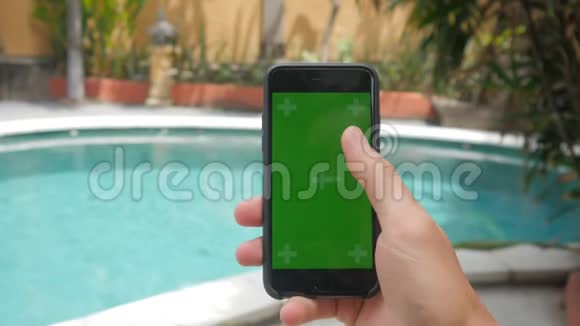 在泳池附近度假时男性用手触摸智能手机的特写镜头绿屏彩色键视频的预览图