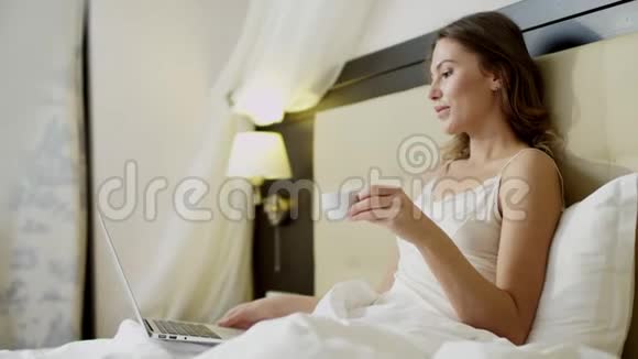 年轻女子在床上一边喝咖啡一边用手提电脑做视频翻译视频的预览图