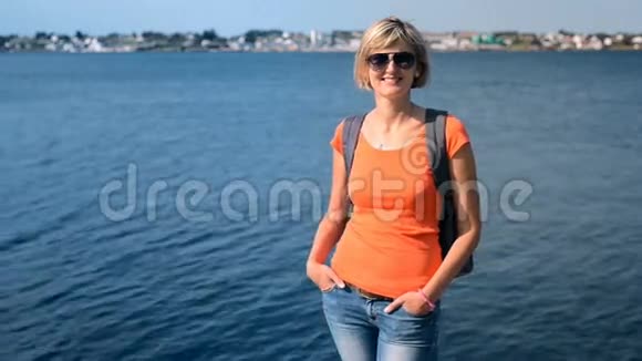 一位背着背包站在海边的休闲妇女头发随风飘扬视频的预览图