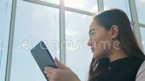 年轻的女乘客在机场一边用平板电脑一边等着她的航班微笑着阳光明媚的一天视频的预览图