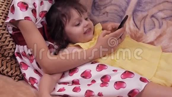 带手机的小女孩姐妹玩手机孩子们正在沙发上玩耍穿裙子的女孩视频的预览图