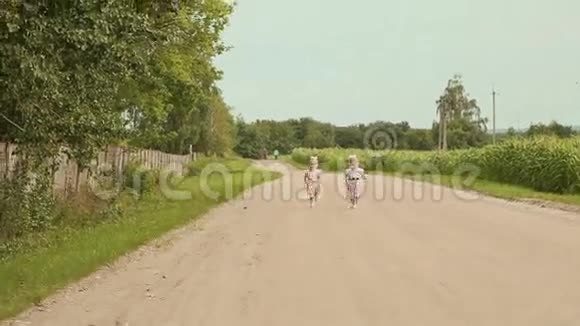 两个小双胞胎姐妹一个接一个地跑在沿路的田野上遥远的森林视频的预览图