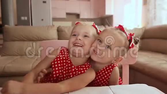 两个可爱的双胞胎姐妹穿着红色的波尔卡多礼服他们一起玩拥抱互相微笑视频的预览图