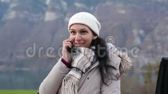 年轻漂亮的女人在阿尔卑斯山的背景上用手机说话视频的预览图