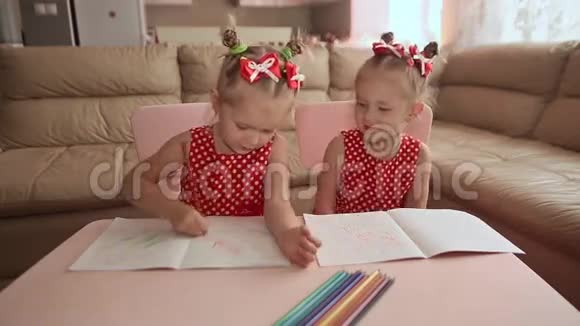 两个微笑的小妹妹双胞胎用彩色铅笔在桌子旁画画视频的预览图