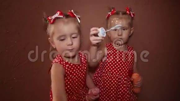 两个漂亮的双胞胎姐妹穿着漂亮的红色连衣裙在房子的房间里一起吹肥皂泡视频的预览图