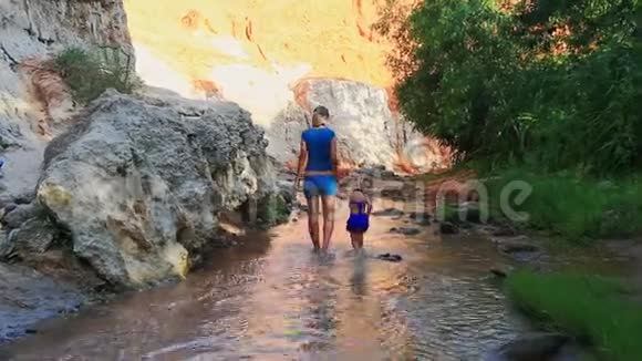 母亲蓝色的小女儿在斜坡的浅溪中散步视频的预览图