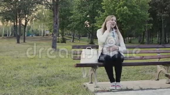 美丽的孕妇通过电话在公园散步视频的预览图
