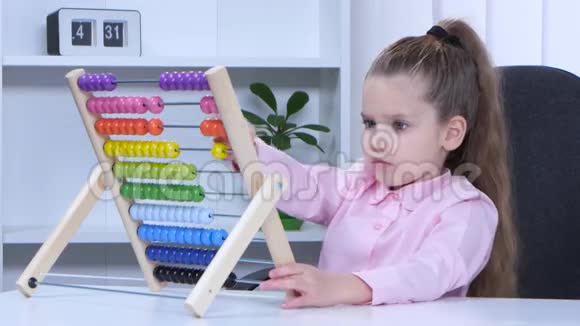 一个穿着衬衫的小女孩坐在桌子旁对五颜六色的ABA说视频的预览图