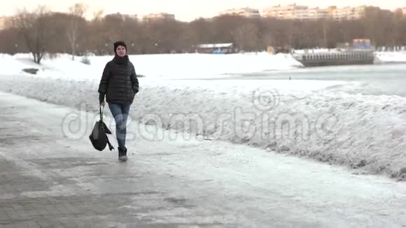 一个手里拿着背包的快乐女孩正在冬天的公园里散步慢动作视频的预览图