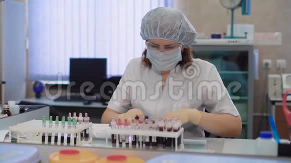 研究助理在白色实验室擦洗防护眼镜面具帽子和手套坐在医疗桌旁视频的预览图