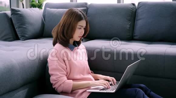 微笑的女人坐在沙发上放松一边浏览网上购物网站视频的预览图