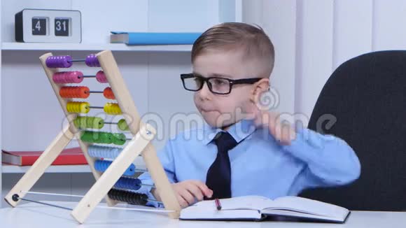 戴眼镜的小男孩考虑账目写在笔记本上视频的预览图