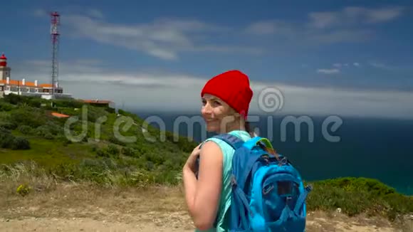一个背着背包的女人在风景如画的丘陵地带来到靠近海洋的灯塔视频的预览图