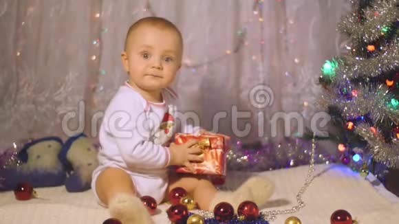 小男孩宝贝在圣诞树的背景下打开圣诞礼物视频的预览图