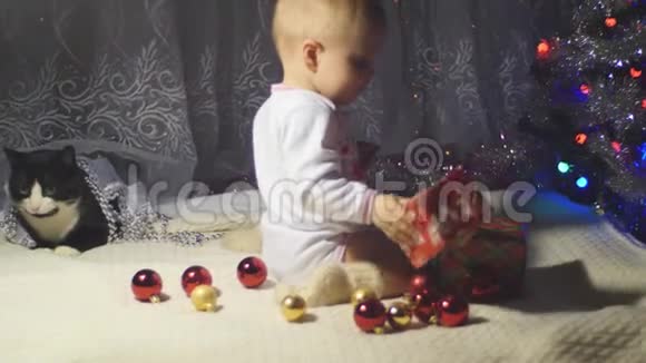 一只婴儿和一只黑白猫坐在圣诞树上放在礼物和玩具中间4k视频的预览图