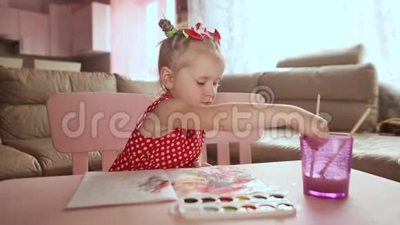 一个穿着红色连衣裙的迷人小女孩在桌子上画着水彩视频的预览图