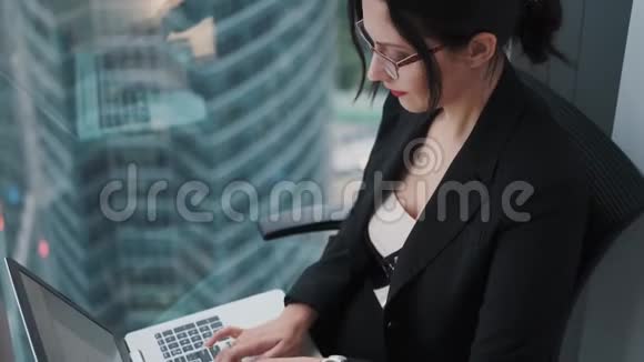 一位年轻的女商人坐在摩天大楼的一层高的窗户旁在笔记本电脑上工作视频的预览图